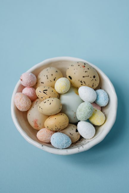Colorful assortment of Easter eggs in a white bowl on a blue background.