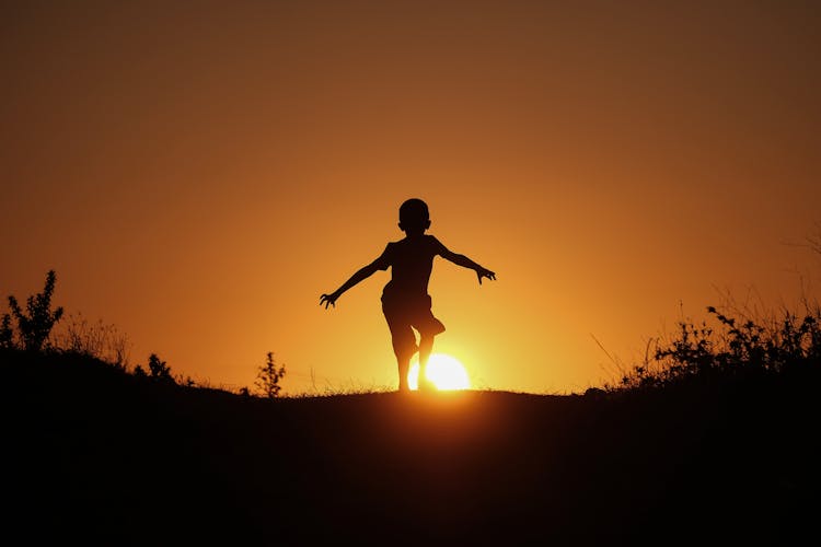 Silhouette Of Child Jumping On Field During Sunset