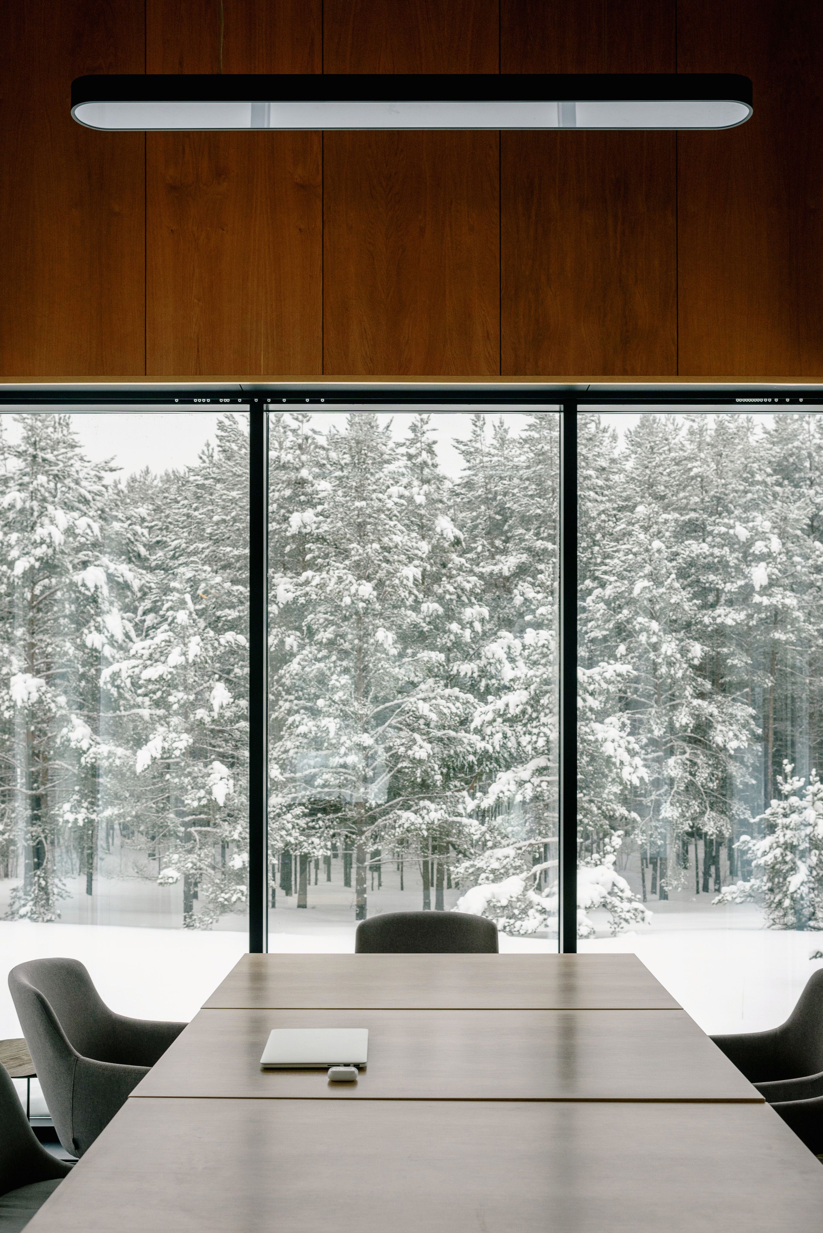 Modern meeting room with large glass windows offering a view of a snowy forest, creating a serene work environment.