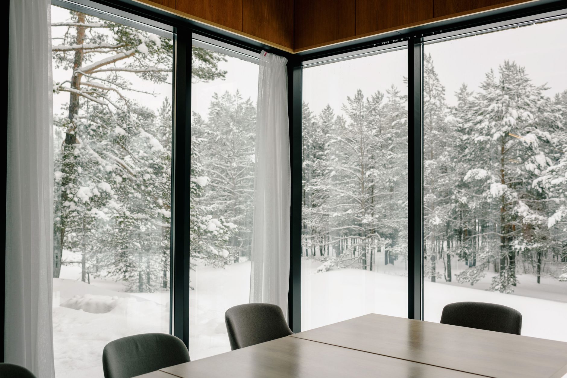 A modern conference room with glass walls offering a stunning view of a snow-covered forest.