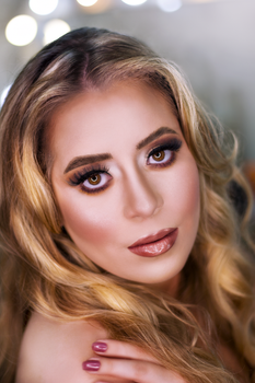 Close-up portrait of a woman with glamorous makeup, blonde hair, and a captivating gaze.