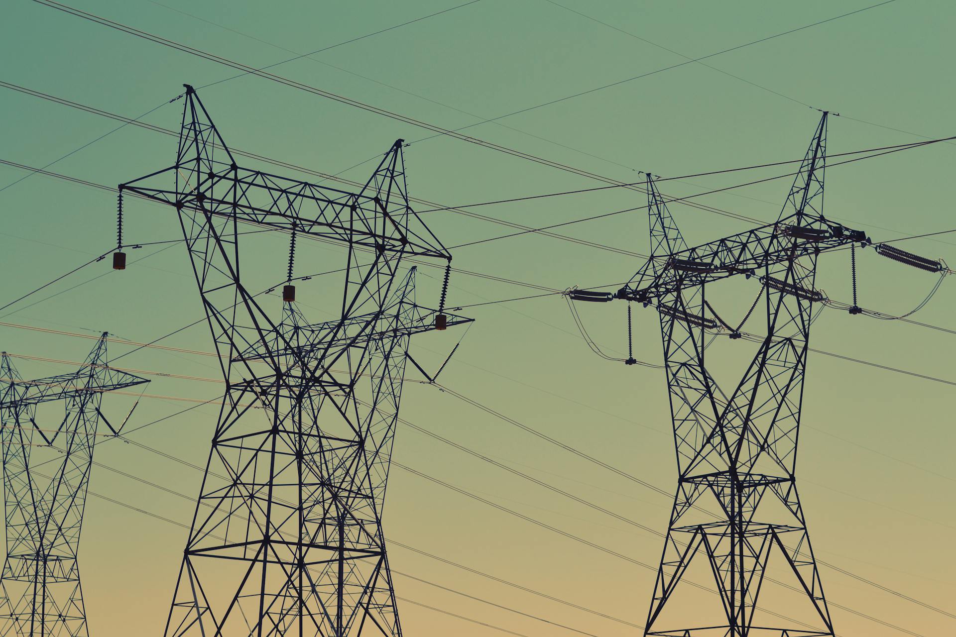 Silhouette of high voltage power lines against a twilight sky, illustrating energy infrastructure.