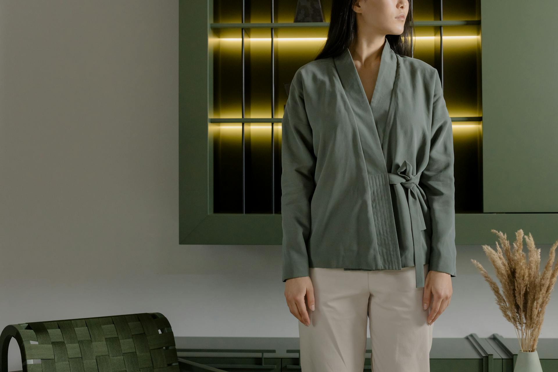 A stylish woman in a green wrap top stands confidently in a chic, modern interior setting.