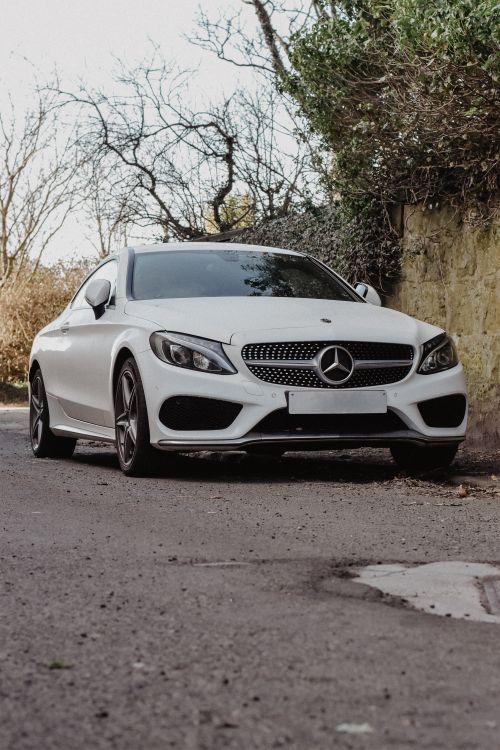 Free A sleek white luxury coupe parked against a rustic stone wall in Scotland's countryside. Stock Photo