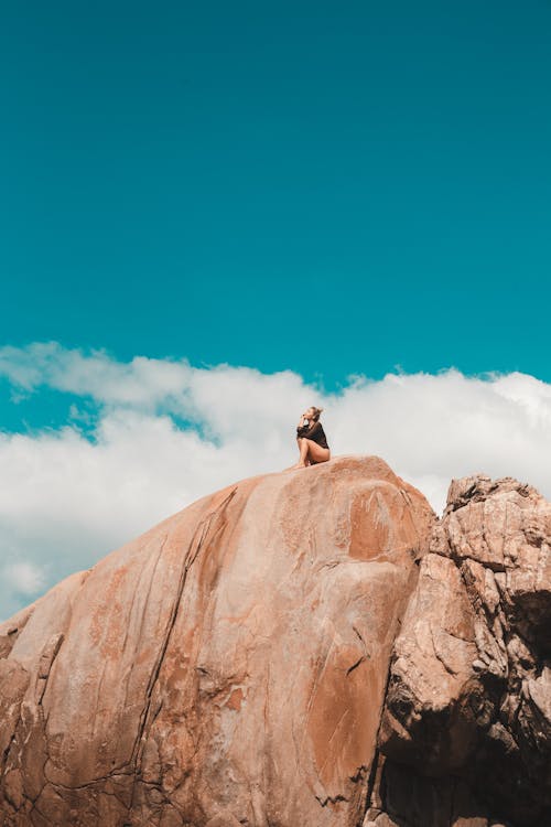 Woman Sitting on Brown Rock Formation Under Blue Sky