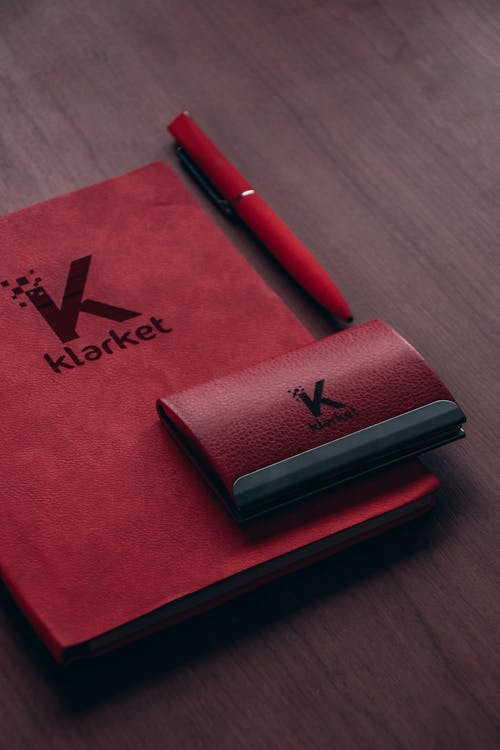Klarket Red Leather Pouch Case and Red Notebook Beside Red Pen