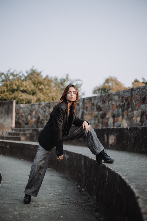 Free Full body of young female in gray trousers and black jacket putting one bent leg on stone stair of old open air theatre Stock Photo