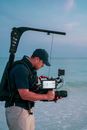Man in Black Shirt and Black Cap Holding Black Camera on Tripod
