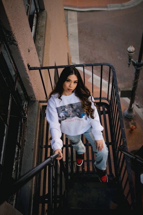 High-Angle Shot of a Woman in White Pullover and Denim Pants Standing on a Staircase