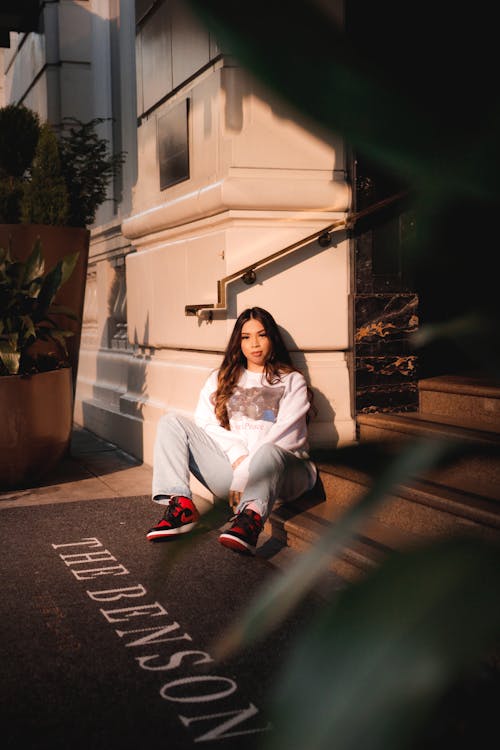 A Woman in White Pullover and Denim Pants Sitting on a Staircase