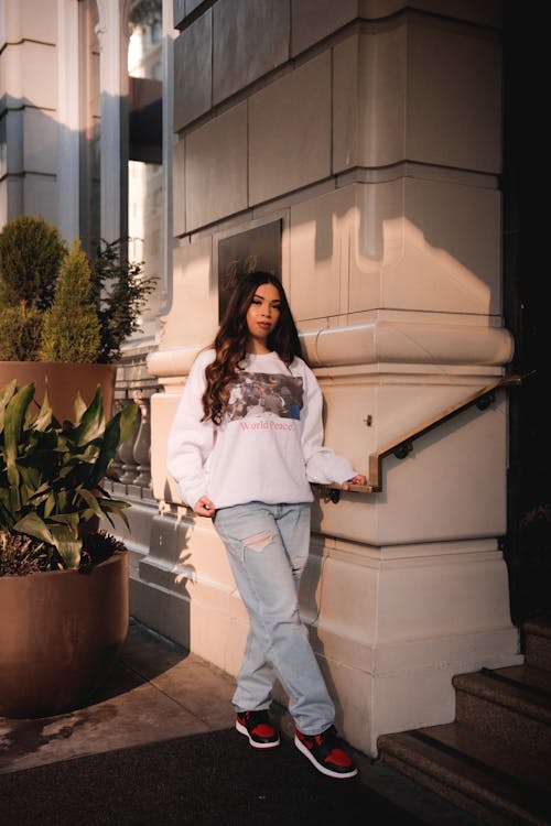 A Woman in White Pullover and Denim Pants Standing Outside