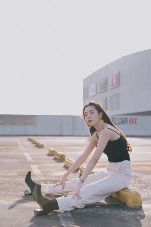 Free A Woman in a Black Tank Top Sitting on a Concrete Parking Block Stock Photo