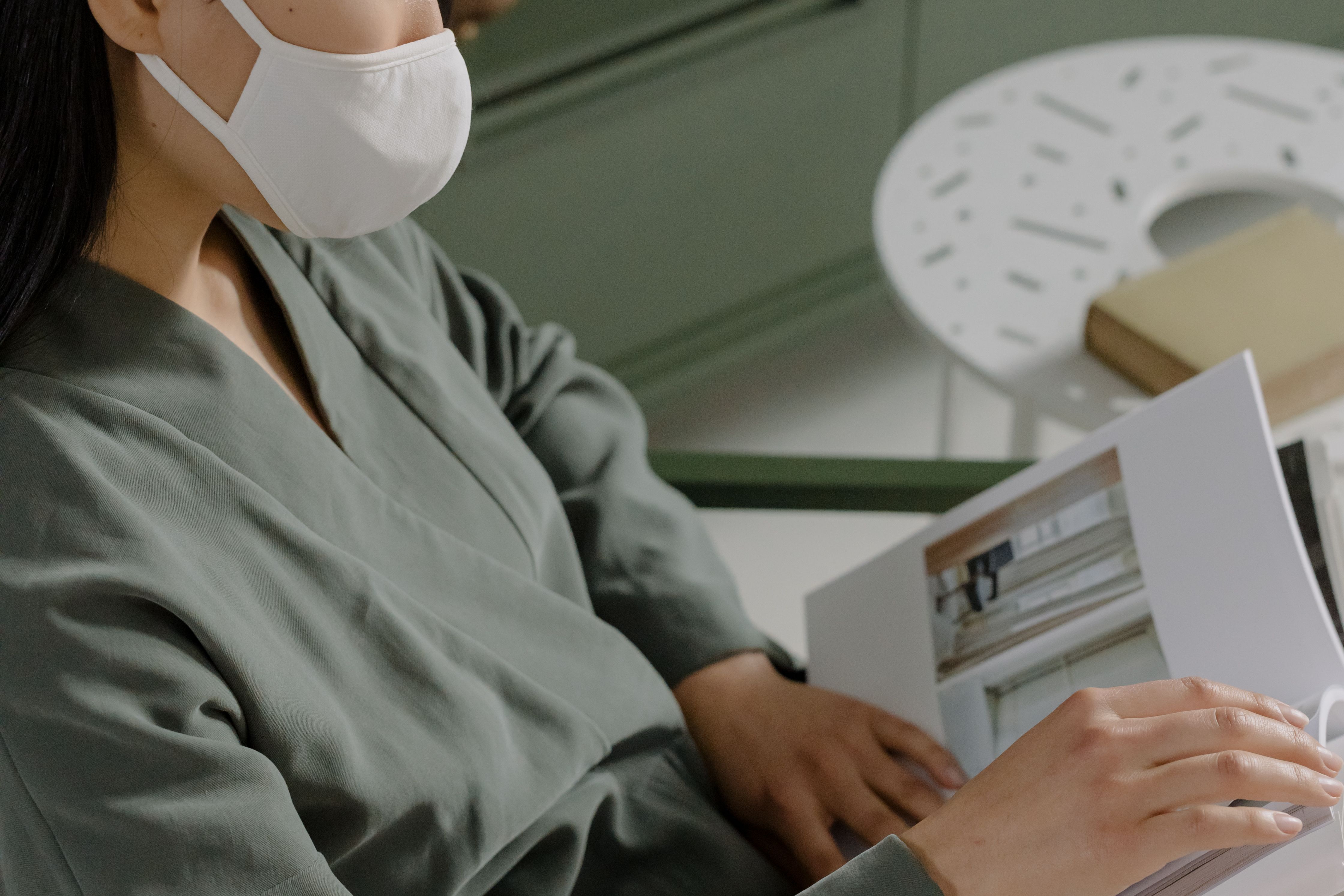 Close-up of a woman in a mask reading a book at home, focused and calm.