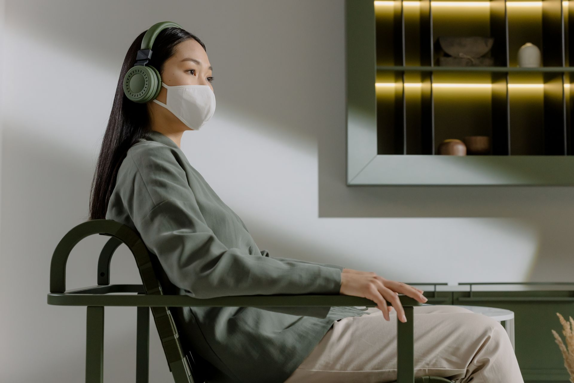 Woman in face mask enjoying music with wireless headphones at home, sitting comfortably and relaxed.