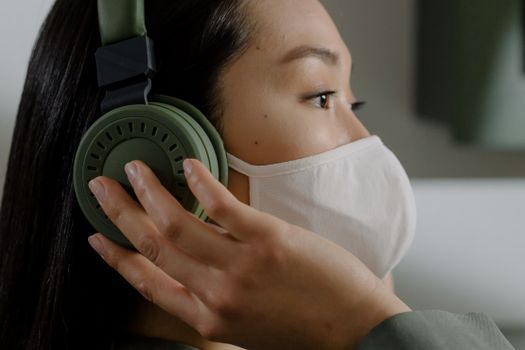 Close-up of a woman wearing a face mask and headphones, listening to music indoors.