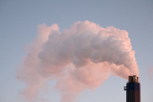 Free From below of clouds of smoke from industrial factory pipes polluting atmosphere against cloudless sky Stock Photo