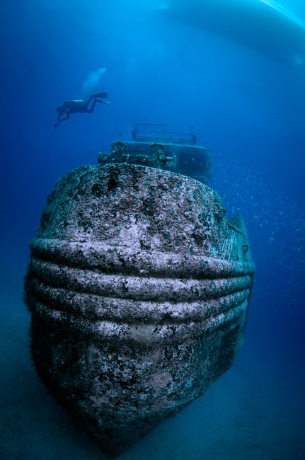 Scuba diver explores a sunken shipwreck in the deep blue ocean, surrounded by marine life.