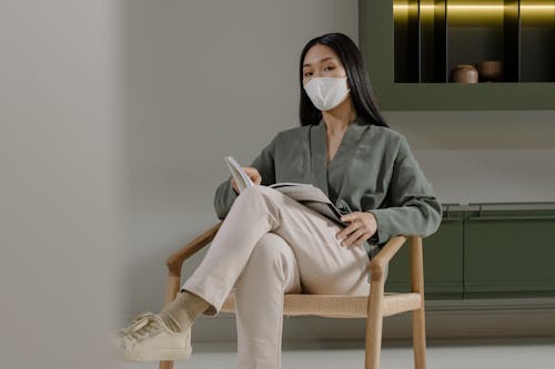 Woman Wearing Face Mask Sitting Holding a Magazine