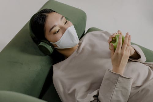 Woman Wearing Face Mask and Headset Holding a Green Apple
