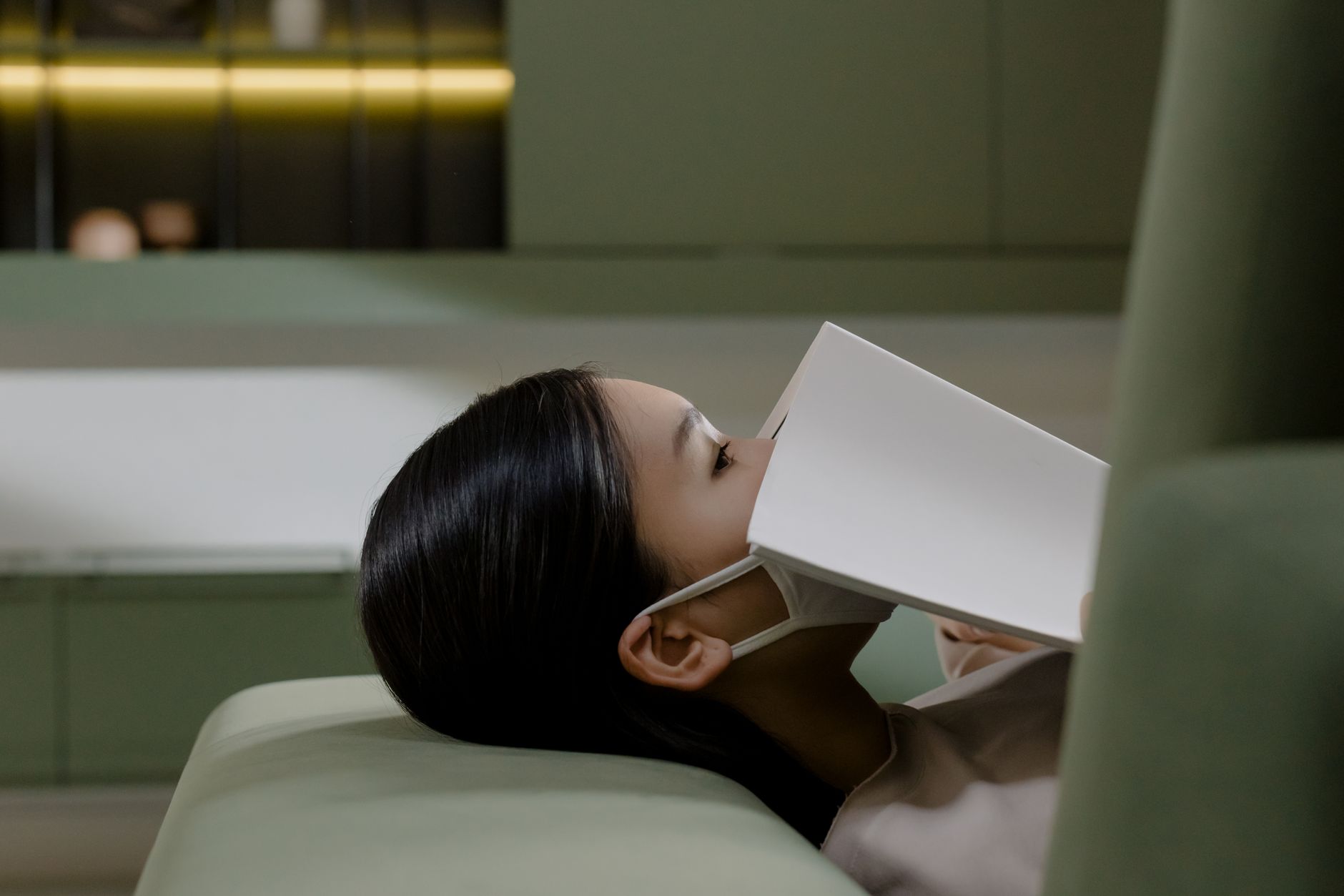 Side view of a woman lying down with a book and face mask in a modern interior.