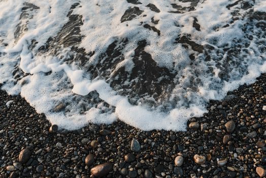 Foamy waves crashing onto a pebbled beach, highlighting the serene coastal texture.