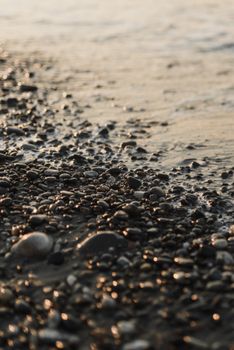 A dark, moody close-up of a rocky seashore with gentle waves at twilight.