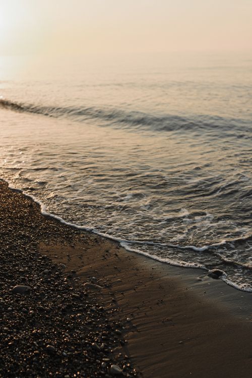 Free Serene ocean waves lapping against a pebble beach at sunset, creating a peaceful atmosphere. Stock Photo