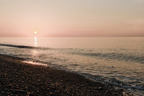 Free Tranquil sunset view over the calm ocean with gentle waves on a pebble beach. Stock Photo