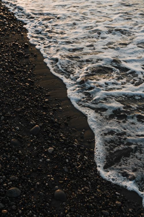 Free A peaceful beach scene with gentle waves and dark sand at sunset, capturing the natural beauty of the seaside. Stock Photo