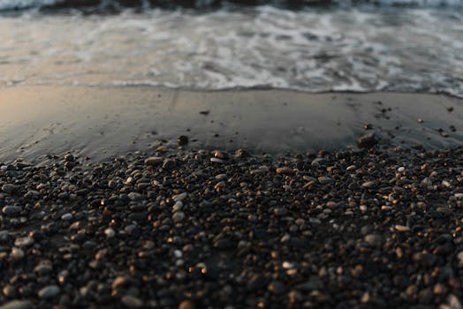 Close-up of wet pebbles on a beach with gentle waves at sunset.