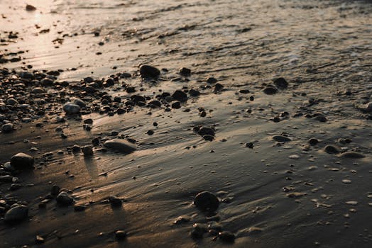 Gentle waves touch a pebble-strewn beach at sunset, creating a serene coastal scene.