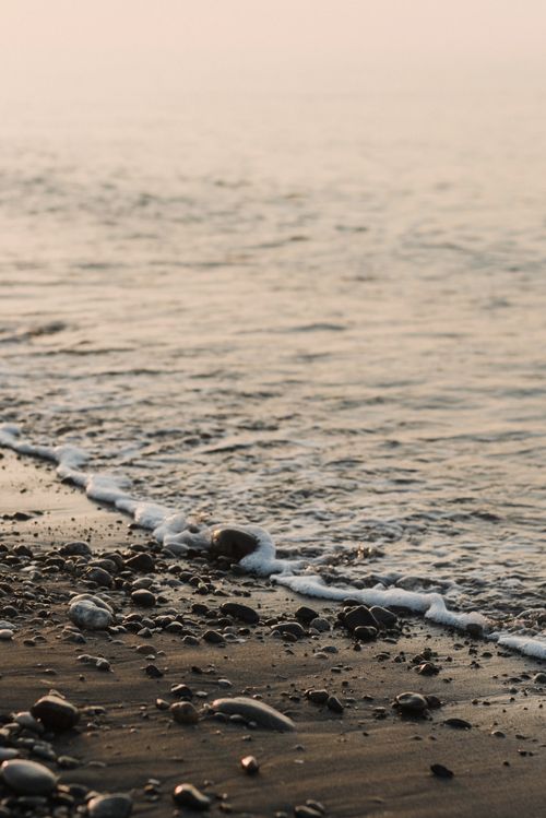 Free A peaceful beach scene with gentle waves and rocky shore at sunset, perfect for nature lovers. Stock Photo