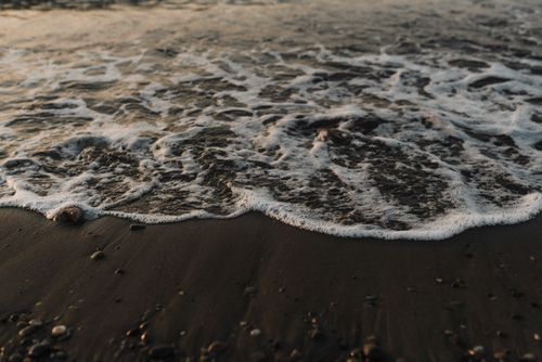 Free Tranquil scene of black sand beach with gentle seafoam waves at sunset, perfect for relaxation themes. Stock Photo