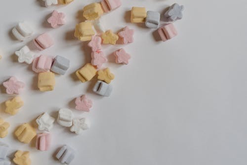 Top view arrangement of multicolored yummy marshmallows in shape of stars scattered in corner of white paper