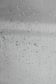 Raindrops on a window glass with a gray and overcast sky creating a moody ambiance.