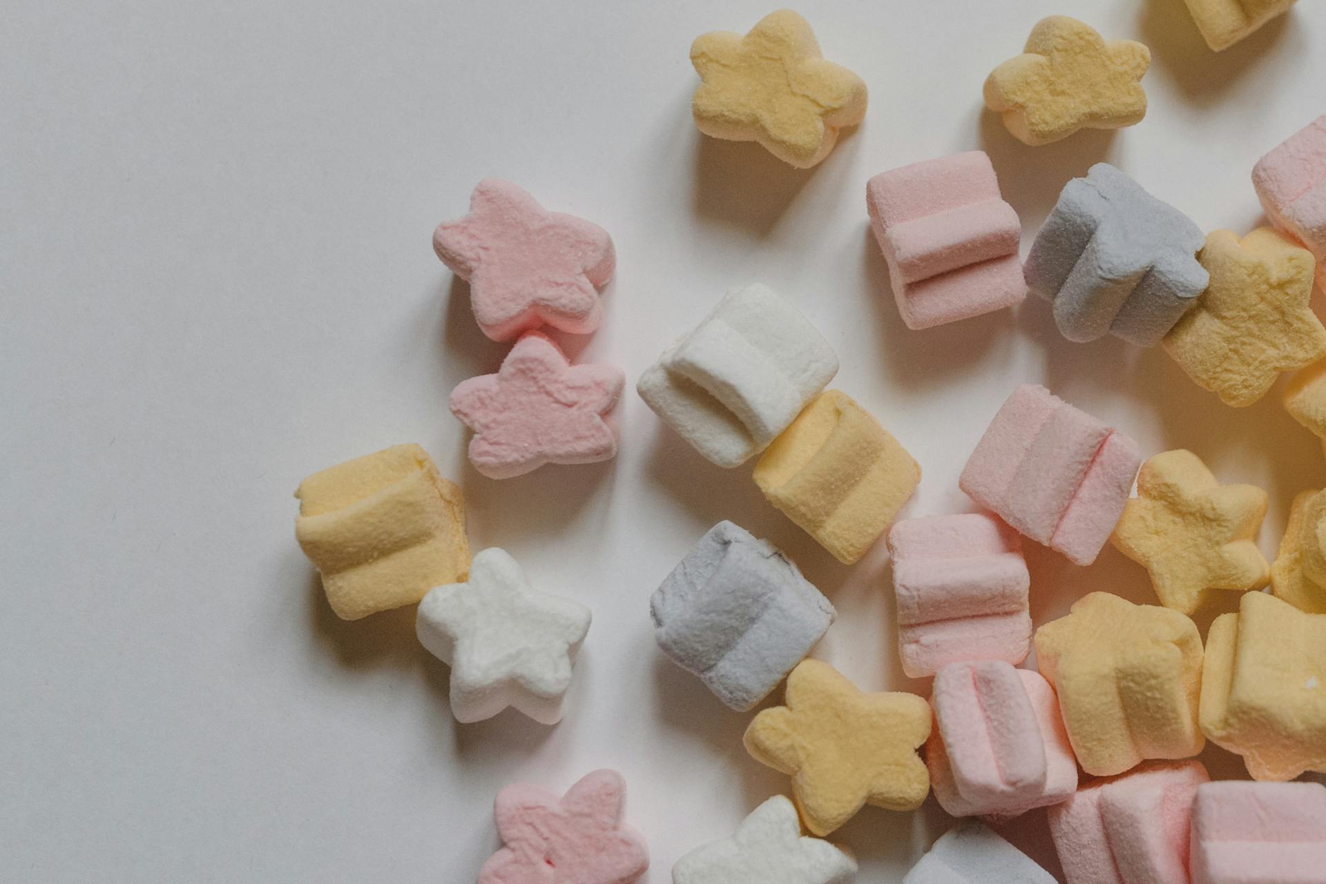 Top view yummy multicolored marshmallows scattered in shape of stars scattered on corner of white table