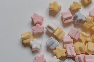 Top view yummy multicolored marshmallows scattered in shape of stars scattered on corner of white table
