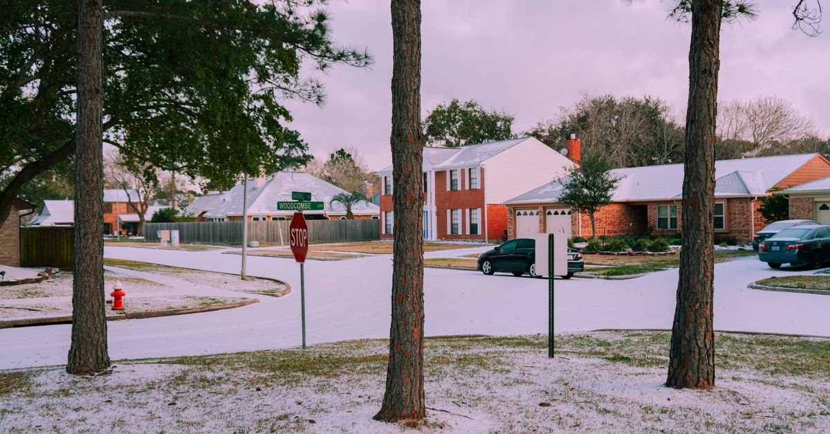 A serene suburban street covered in snow, featuring houses and trees on a winter day.