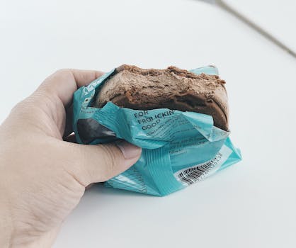 Close-up of a hand holding a chocolate ice cream sandwich in turquoise packaging.