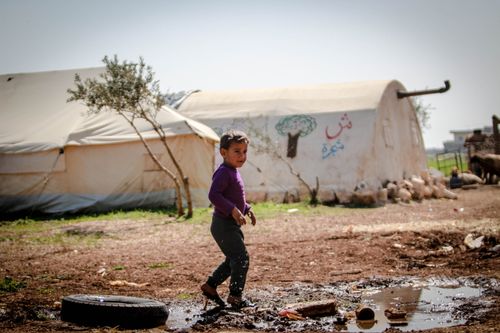 Free A young boy in a purple shirt walks through a muddy area in a Syrian refugee camp, reflecting resilience and hope. Stock Photo