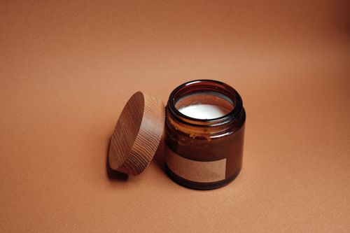 Free A brown jar with an open lid and candle inside on a brown background, perfect for relaxation themes. Stock Photo