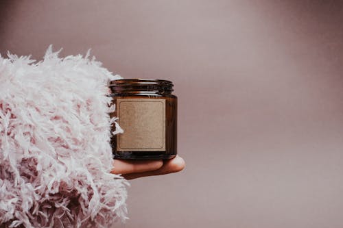 A Person Holding a Candle Brown Glass Container