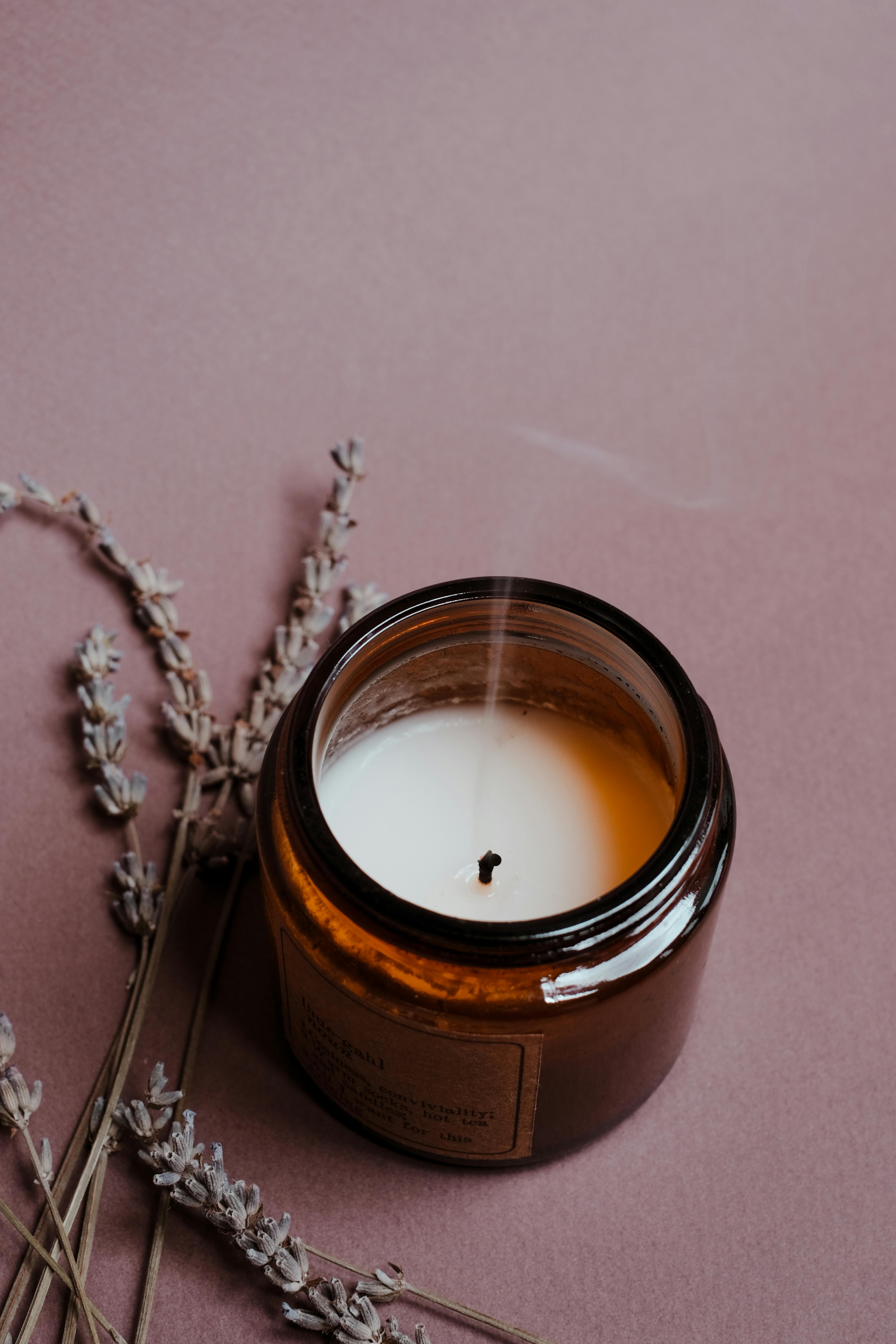 Organic candle in amber jar with lavender on a minimalist pink background, exuding a calming aroma.