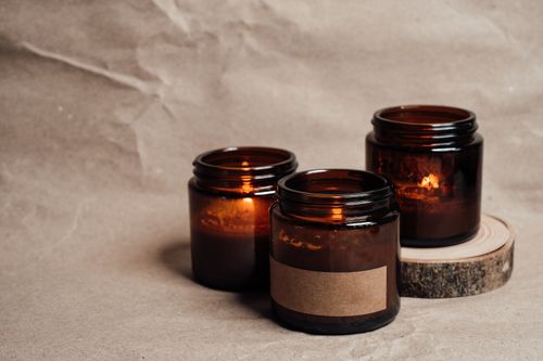 Free Warm glow of candles in glass jars creating a cozy atmosphere on a neutral background. Stock Photo