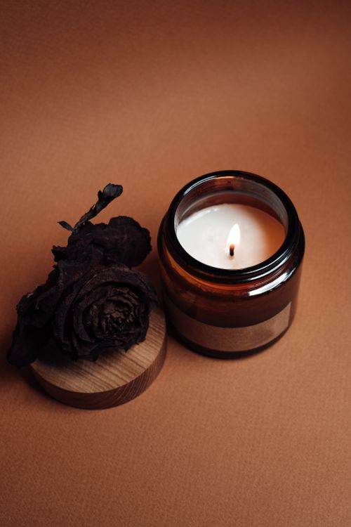 Free A close-up of a lit candle in a jar beside a dried flower on a wooden surface. Stock Photo
