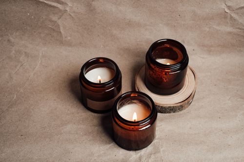 Free Warm ambient candles glowing in brown glass jars on a textured paper surface. Stock Photo