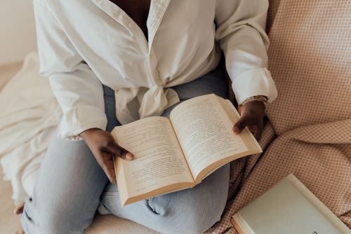 Free A person enjoys a peaceful reading moment with an open book on a couch, indoors. Stock Photo