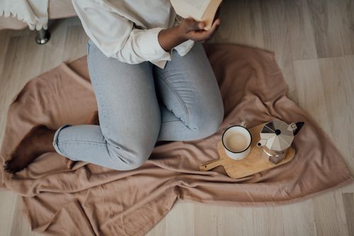 Free Person reading book with coffee and moka pot on cozy blanket indoors. Stock Photo