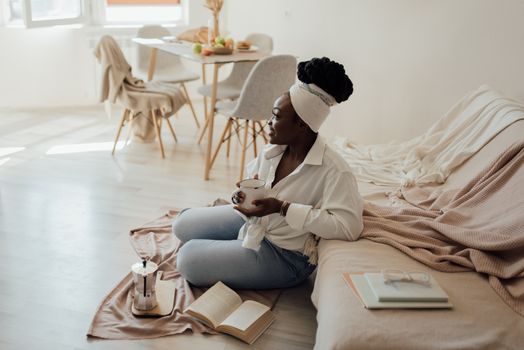 A woman enjoying a cup of coffee in a bright living room setting, surrounded by books and natural light.