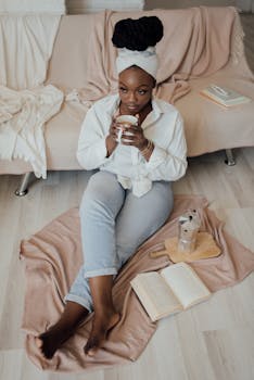 Woman enjoying a morning with coffee, books, and cozy blankets on a living room floor.